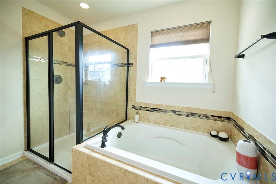 Black-framed glass shower enclosure, integrated soaking tub, tiled shower surround, recessed lighting, and a single window with roller shade