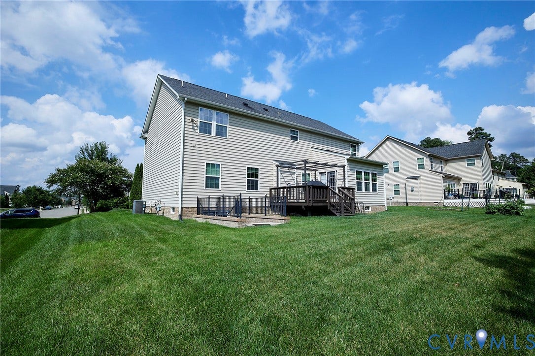 Spacious backyard featuring a multi-level deck with a pergola, mature landscaping, and light-toned siding