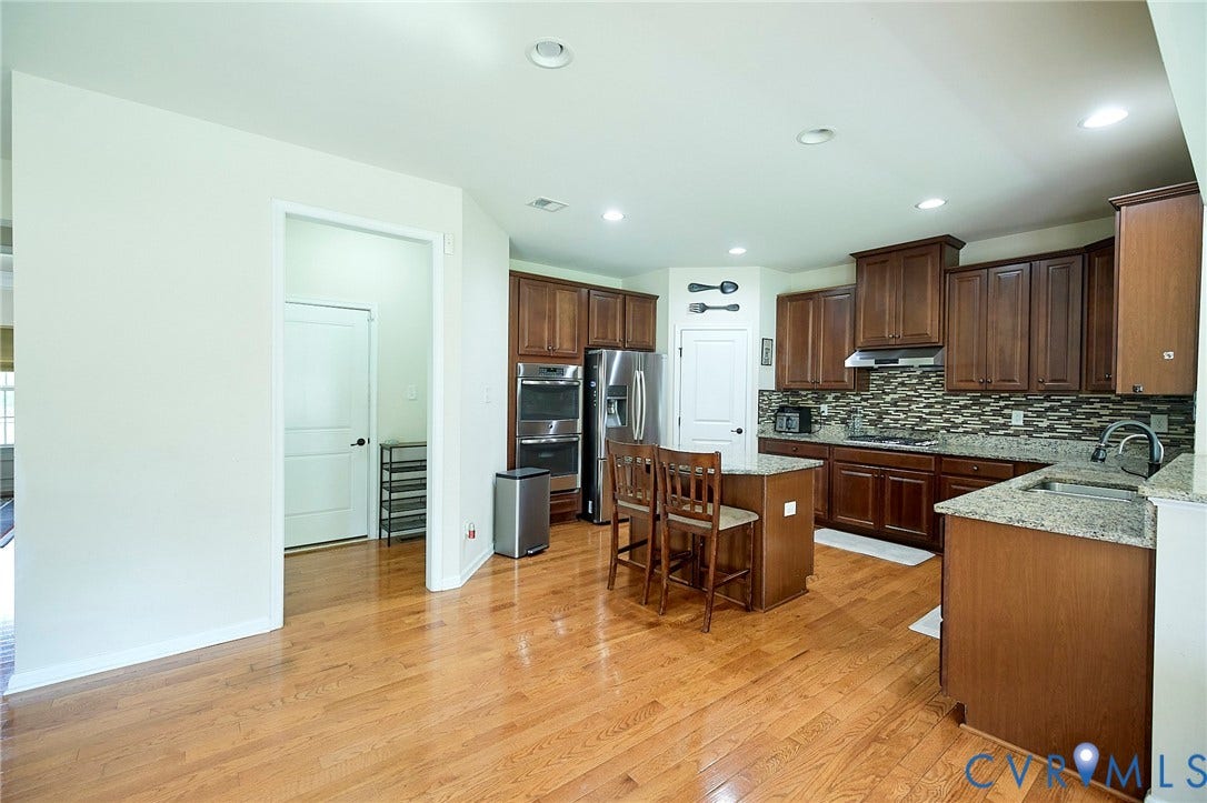 Kitchen featuring wood-finish flooring, dark wood cabinetry, granite countertops, and stainless steel appliances