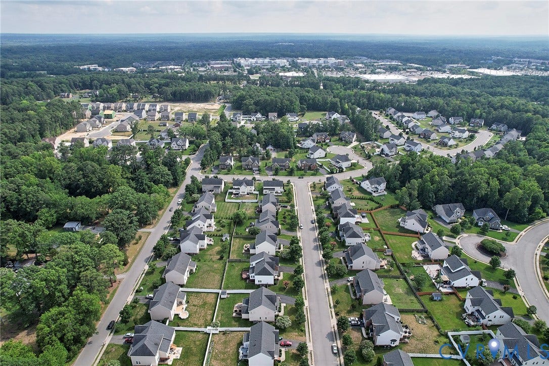 Aerial perspective of a residential community featuring detached homes, paved streets, and surrounding mature trees
