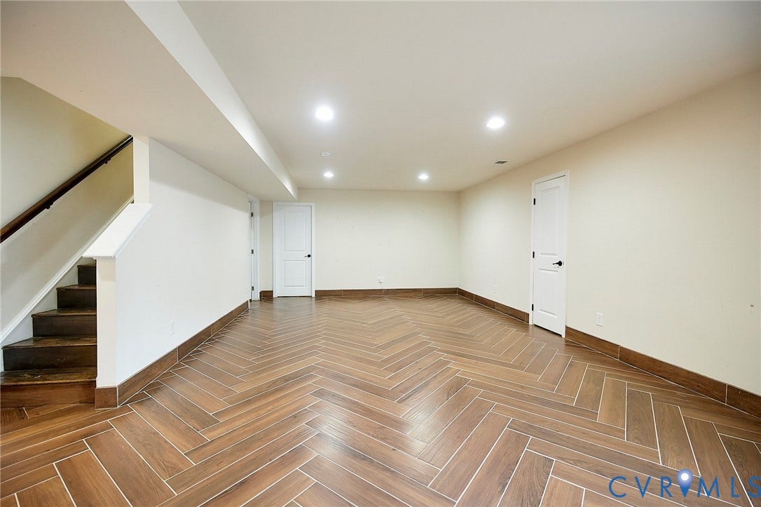 Spacious room featuring herringbone-pattern wood-finish flooring, recessed lighting, and white paneled doors