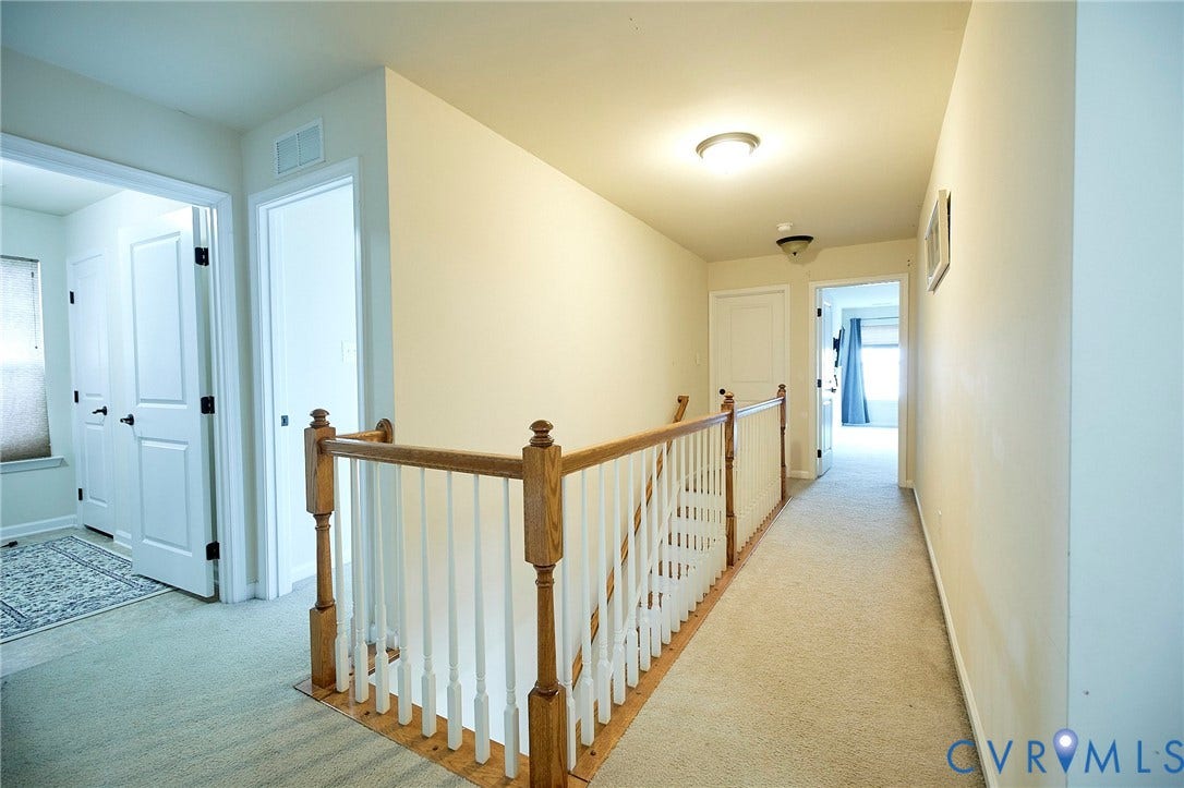 Carpeted hallway featuring a wood and white spindle staircase railing, flush mount ceiling lighting, and panel doors