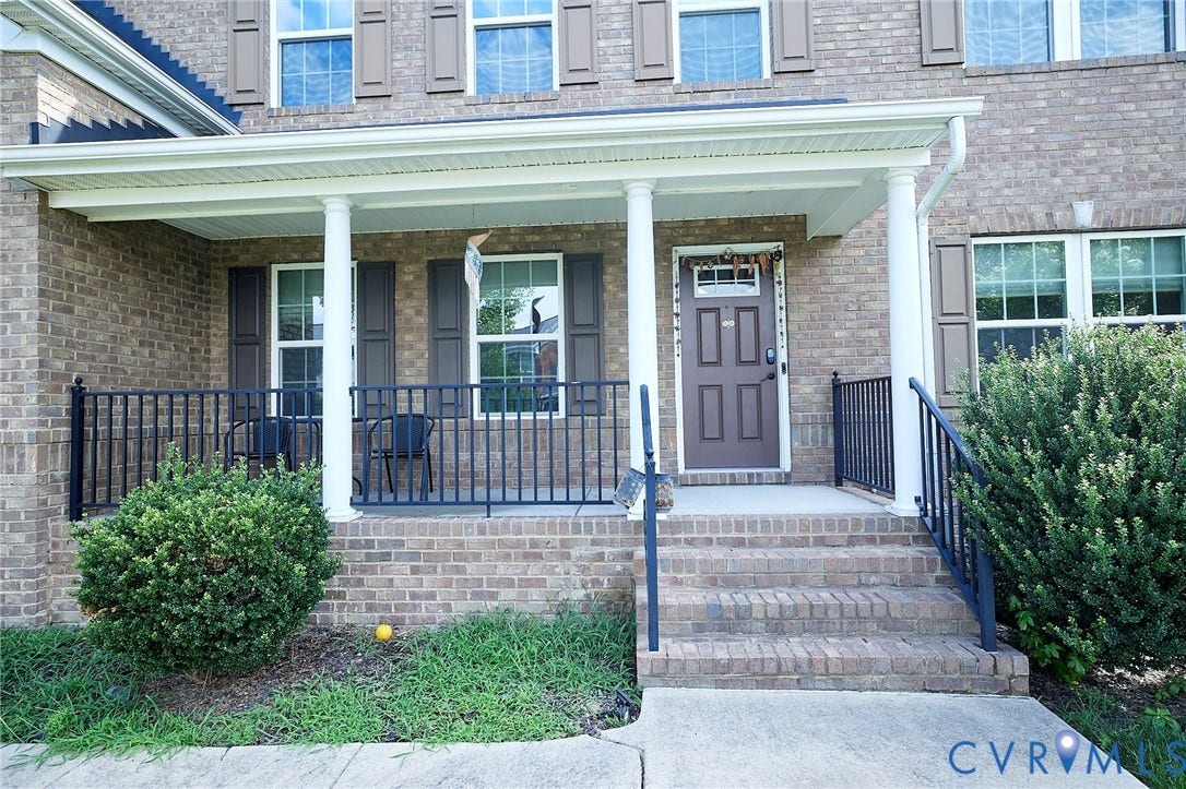 Brick exterior with a covered porch featuring white support columns, black railings, and a multi-pane front door