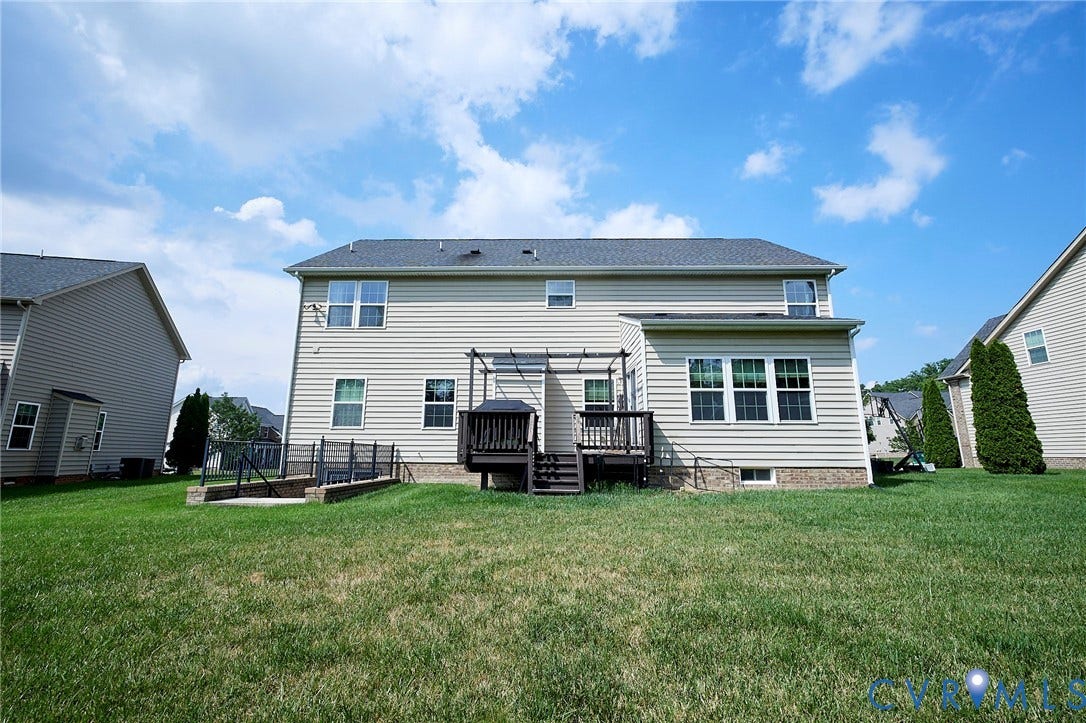Expansive rear lawn, multi-level composite deck with pergola, and a lower-level concrete patio with a retaining wall