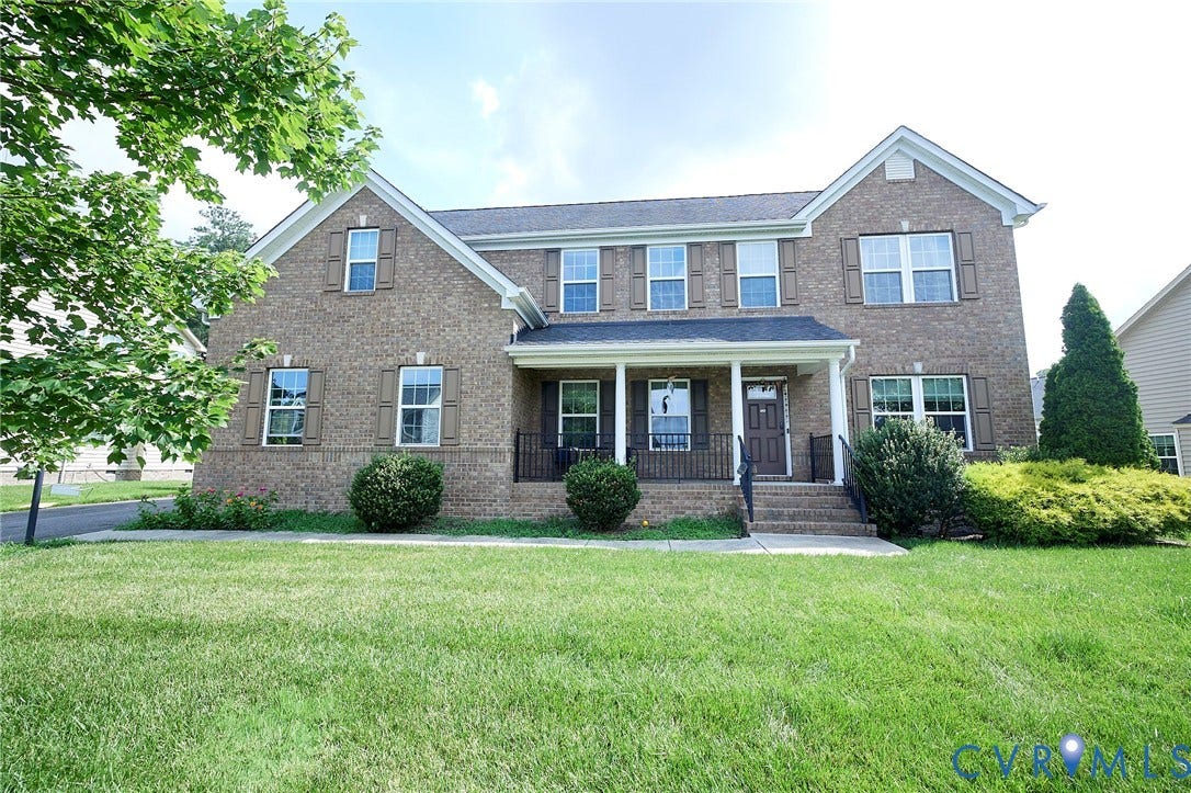 Brick exterior with multiple gables, covered porch, dark entry door, and uniform landscaping