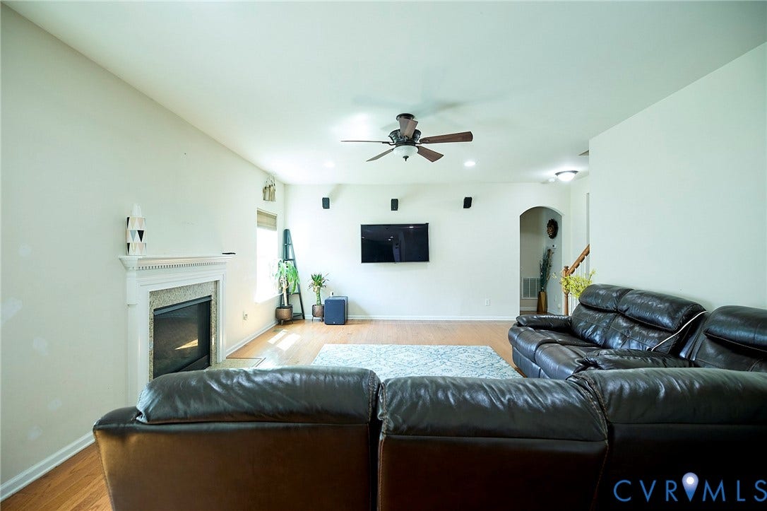 Living area featuring wood-finish flooring, a fireplace with a white mantel, and an arched doorway