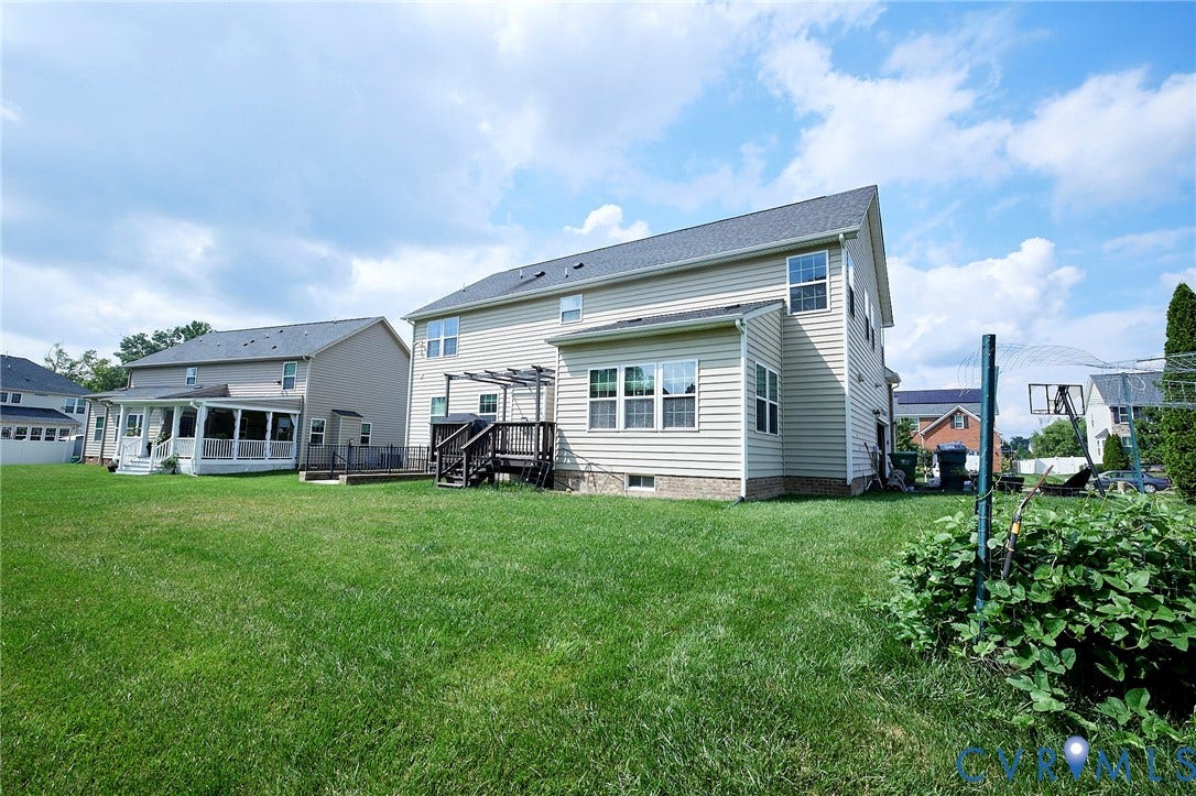 Expansive backyard featuring a lush lawn, two-story residence with light-colored siding, and a multi-level deck with pergola