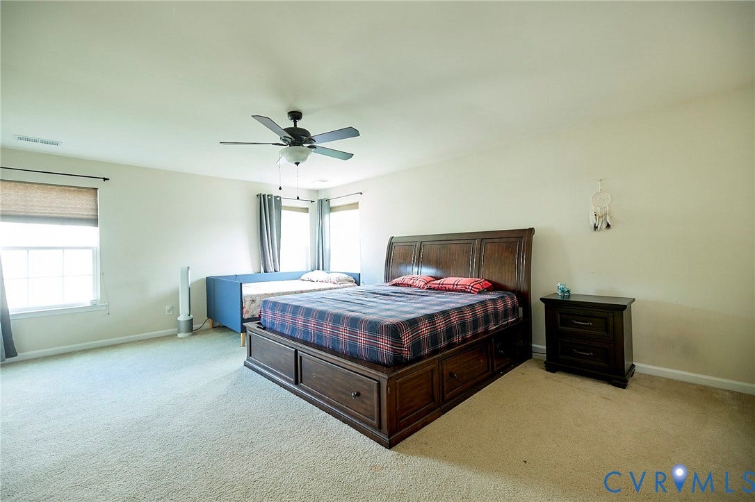 Spacious room featuring light neutral wall paint, light-colored carpeting, multiple windows, and a ceiling fan with integrated lighting