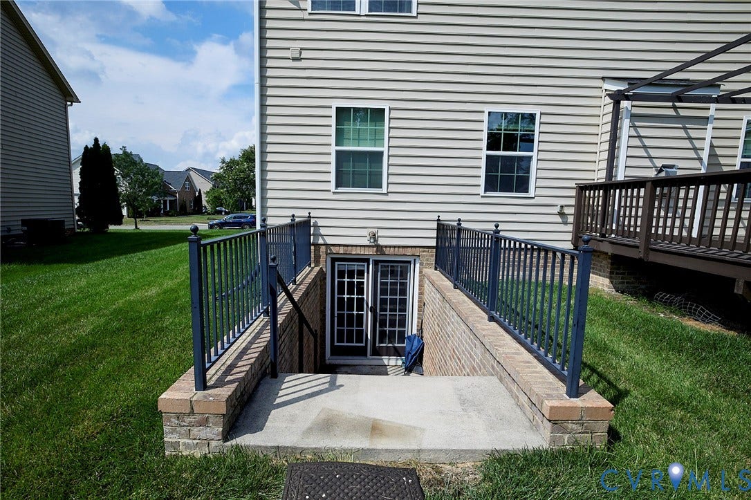 Walk-out basement access featuring a concrete patio, brick retaining walls, and black metal railings