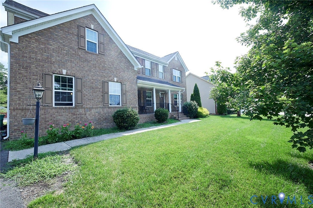 Brick exterior featuring white window frames with dark shutters, a covered porch with white columns, and a large lawn