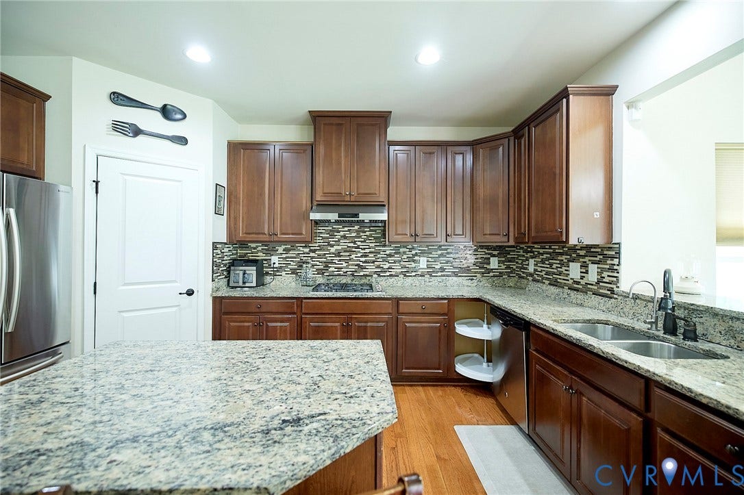 Kitchen featuring wood-finish flooring, recessed lighting, wood cabinetry, stone countertops, and a tile backsplash