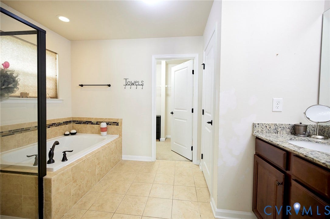 Tile flooring, built-in bathtub with tile surround, glass-enclosed shower, wood vanity with granite countertop, and recessed lighting