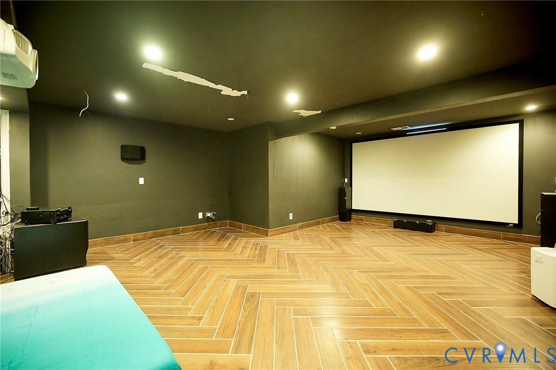 Herringbone wood-finish flooring, recessed ceiling lighting, large projector screen, and dark wall finishes