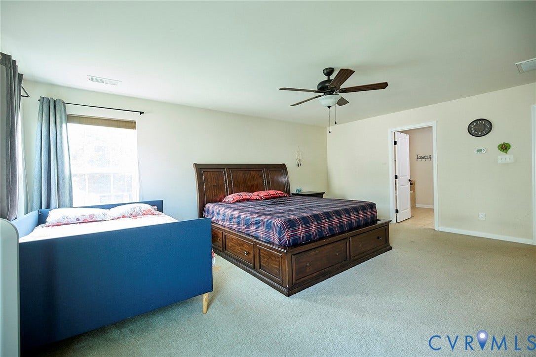 Light-colored wall paint, ceiling fan with light fixture, carpeted flooring, and a door frame leading to another room