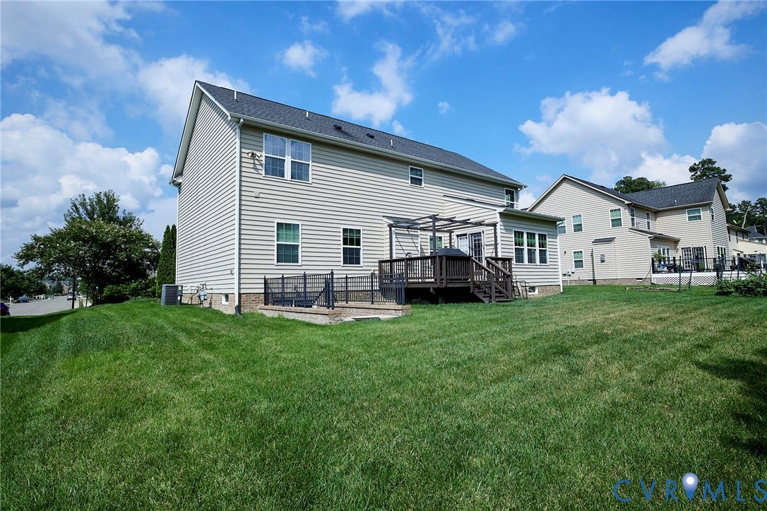 Expansive backyard with a manicured lawn, multi-level wood deck, and a ground-level patio with black metal fencing