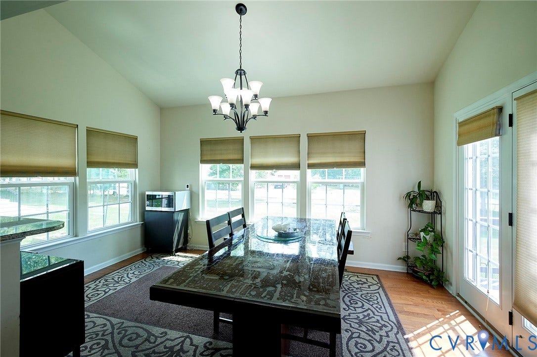 Vaulted ceiling, wood-finish flooring, multiple windows with blinds, and a multi-light chandelier