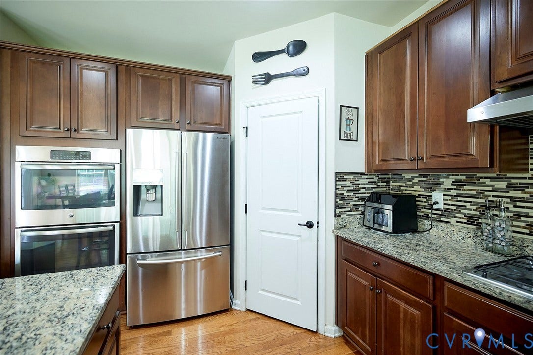 Hardwood flooring, granite countertops, stainless steel appliances, dark wood cabinetry, and a mosaic tile backsplash