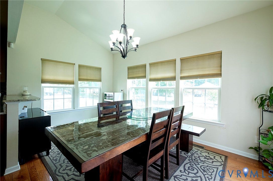 Vaulted ceiling with an iron chandelier, four large windows, wood-finish flooring, and a half-wall featuring a countertop