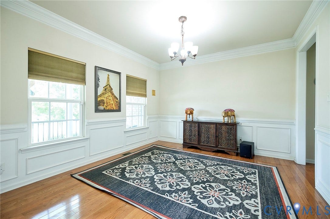 Hardwood flooring, decorative wall paneling, crown molding, two windows, and a ceiling-mounted light fixture