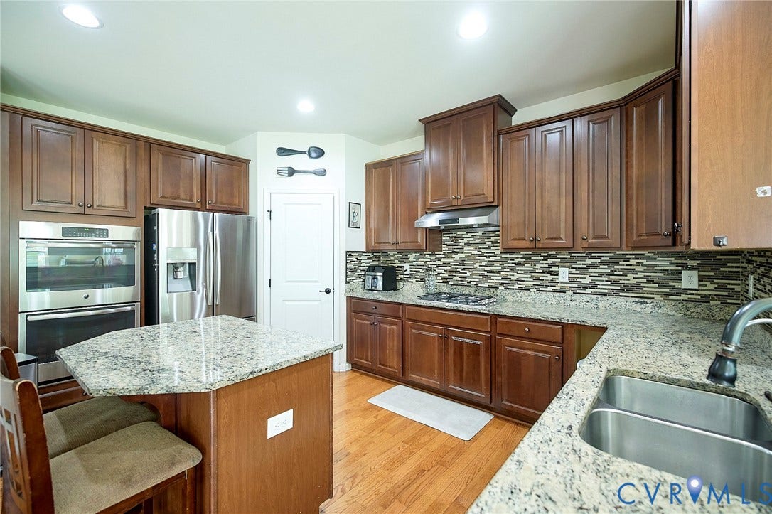 Kitchen featuring wood-finish flooring, stone countertops, stainless steel appliances, wood cabinetry, and a mosaic tile backsplash