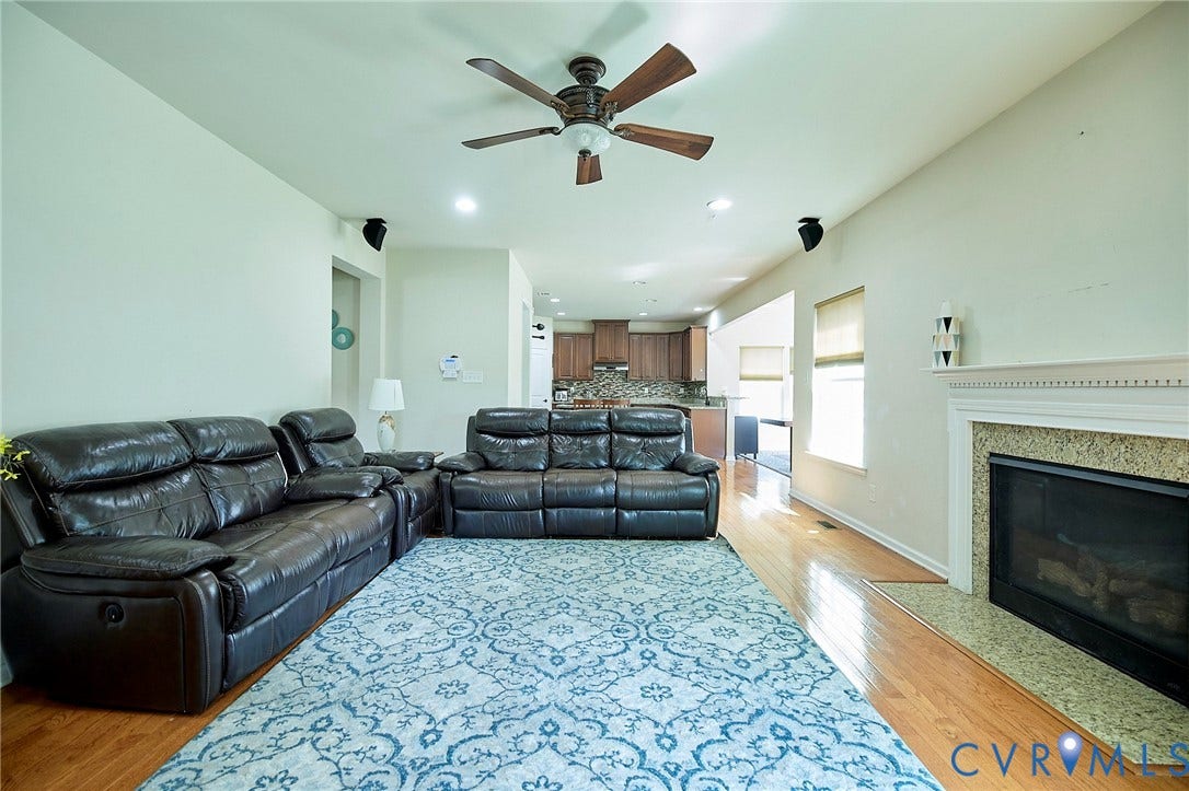 Hardwood flooring, ceiling fan, recessed lighting, and a fireplace with a stone surround