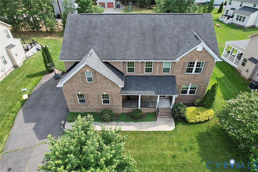 Brick facade residence featuring a covered front porch, gabled rooflines, a paved driveway, and manicured landscaping