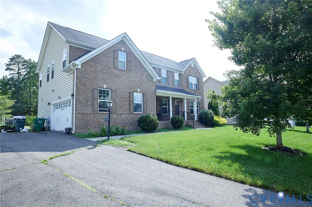 Brick and siding exterior with a covered porch, attached two-car garage, and established landscaping