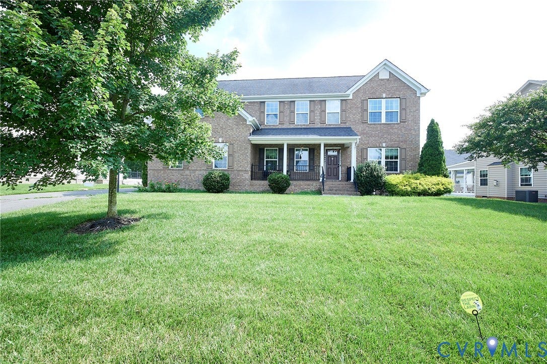 Brick facade residence with a columned front porch, front yard landscaping, and mature trees