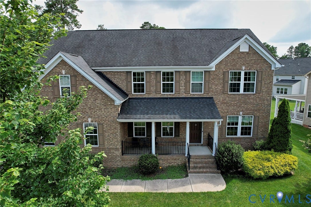 Brick facade colonial with a covered porch entry, dark shingle roof, white window frames, and decorative shutters