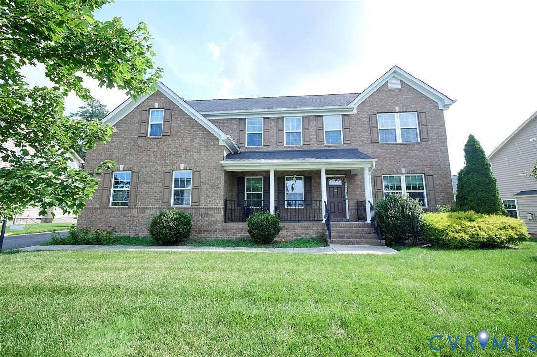 Brick exterior with a covered porch, multiple windows, and a landscaped front yard