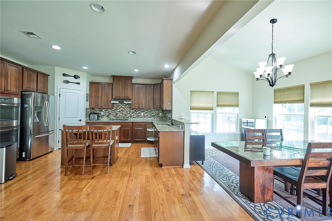 Open-concept kitchen and dining area featuring wood-finish flooring, recessed lighting, and a vaulted ceiling
