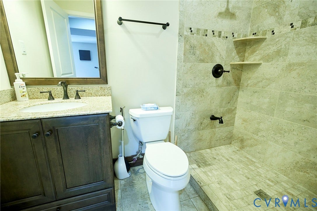 Walk-in shower with tiled walls and floor, corner shelving, and dark bronze fixtures