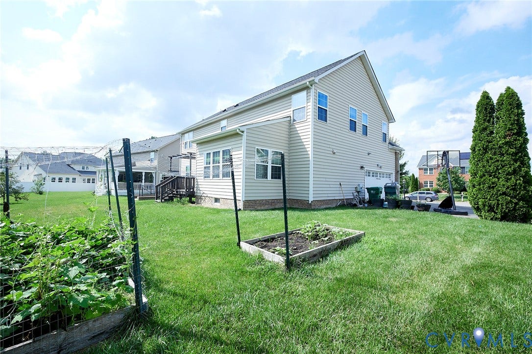 Expansive rear yard featuring green lawn, established garden beds, and a multi-level siding exterior