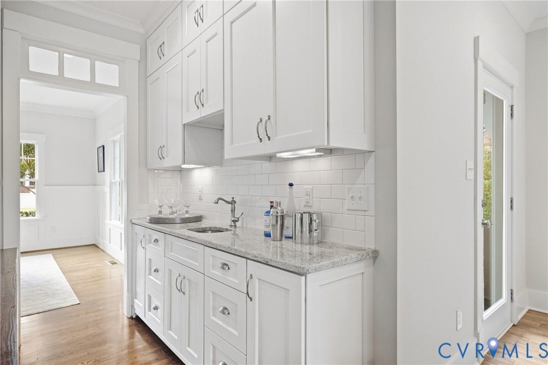 Built-in wet bar featuring white shaker-style cabinetry, a polished countertop, undermount sink, and subway tile backsplash