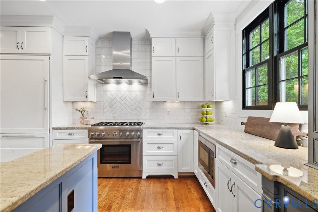 White shaker cabinetry with undermount lighting, stainless steel appliances, herringbone tile backsplash, light-toned granite countertops, and wood-finish flooring