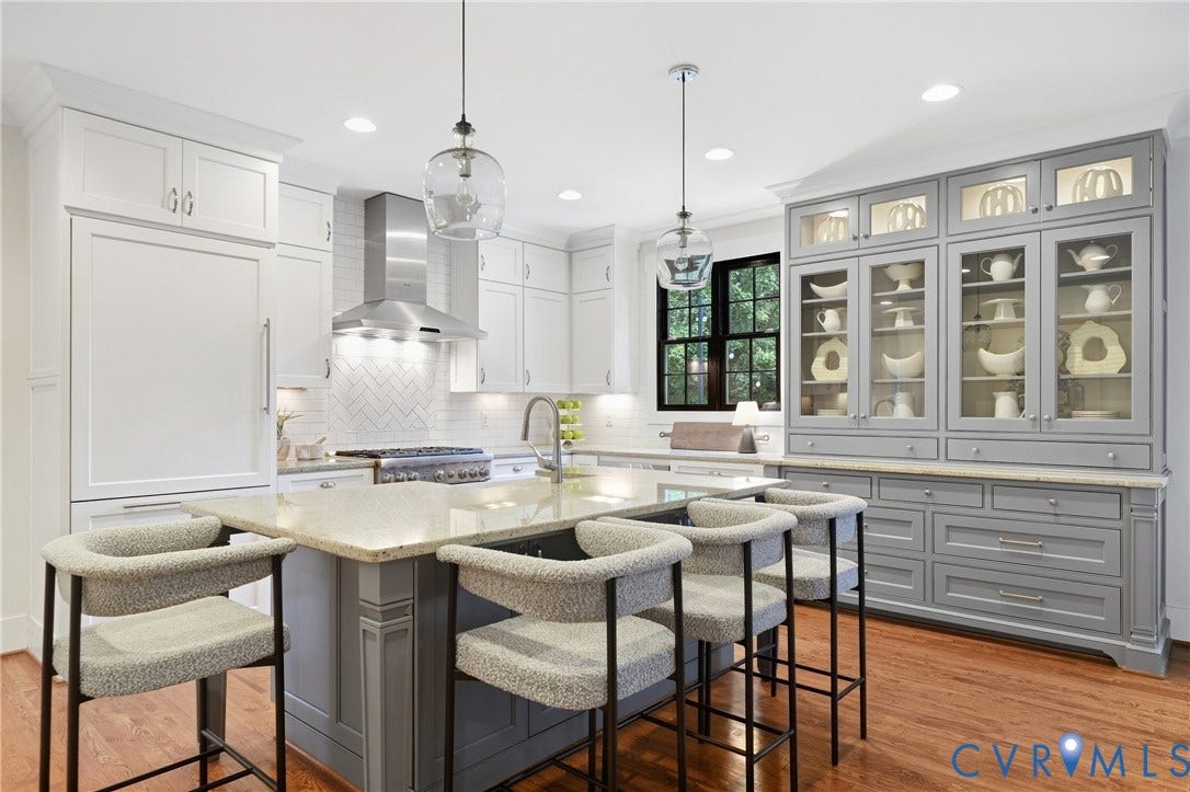 Kitchen featuring a central island with countertop seating, white shaker cabinetry, a stainless steel range hood, a herringbone tile backsplash, and a built-in display cabinet with glass doors