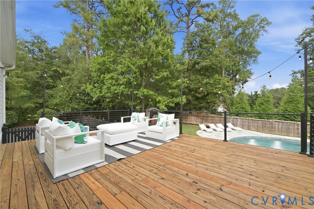 Spacious wood deck with black metal railing, overlooking a curved in-ground swimming pool and private backyard