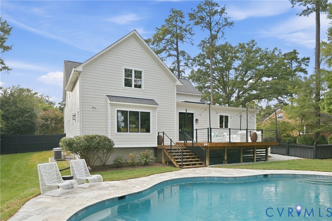 White siding exterior with a multi-level wood deck, black metal railing, and an in-ground swimming pool featuring a flagstone surround