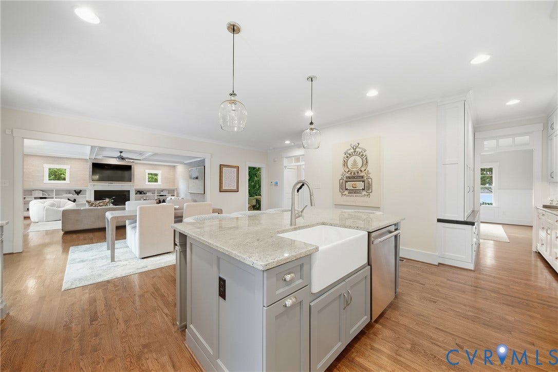 Kitchen island with a farmhouse sink, stainless steel dishwasher, and light-toned stone countertop