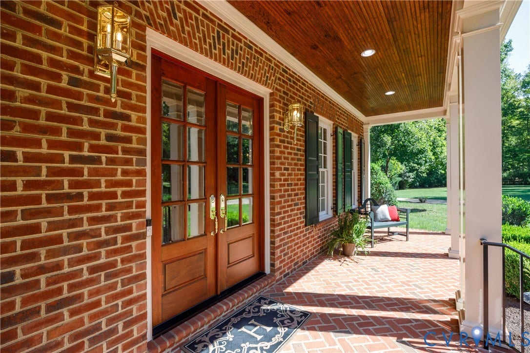 628 Cedar Run Road, Hermitage Country Club Area, Manakin Sabot, VA 23103 The covered front porch features a wood-paneled ceiling, double entry doors with glass panels, and a herringbone-patterned brick porch.