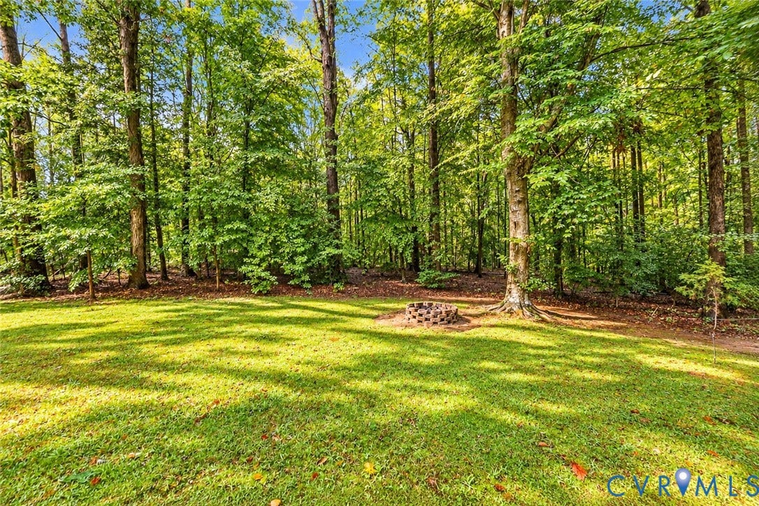 Expansive grassy area surrounded by mature trees, featuring a stone-lined fire pit