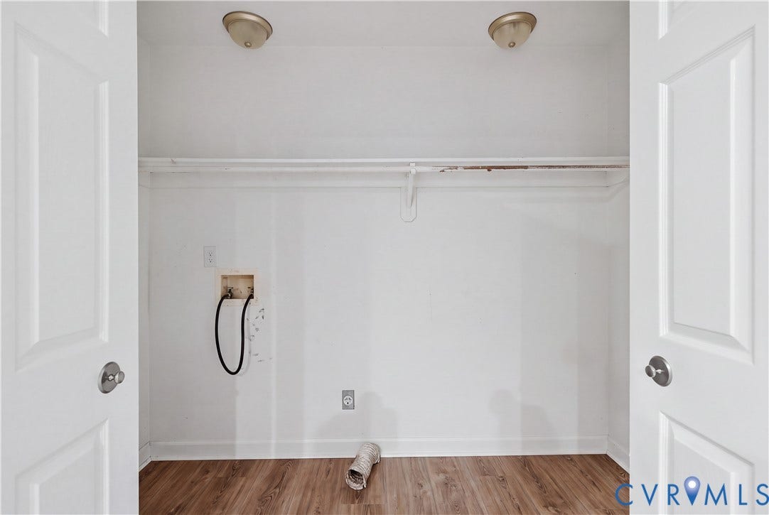 Laundry area with wood-finish flooring, white walls, and a built-in shelf with hanging rod