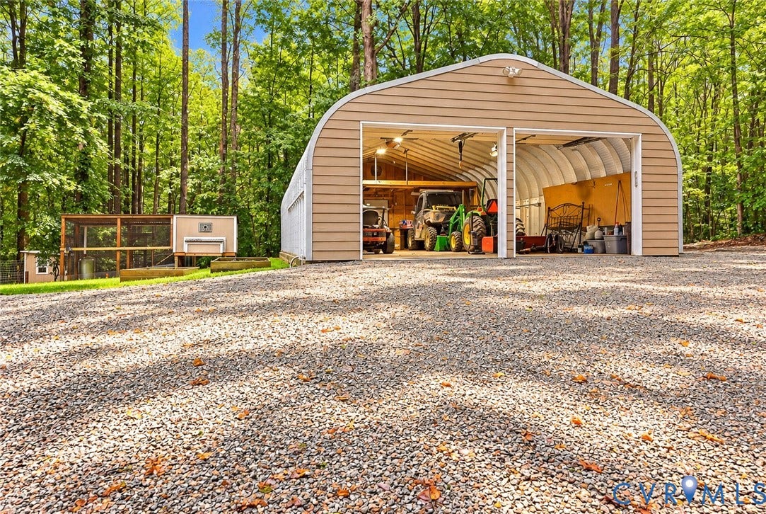 Two-bay metal garage with roll-up doors, gravel driveway, and a fenced enclosure