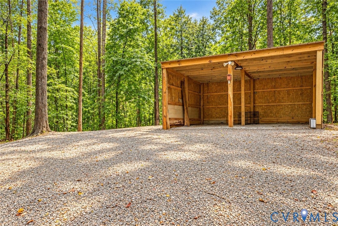 Gravel parking area with a wood-frame shelter, featuring a metal roof and oriented strand board walls