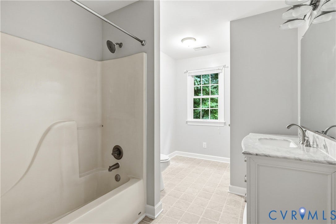 Bathtub with shower, vanity with integrated sink, polished chrome faucet, window, and tiled flooring
