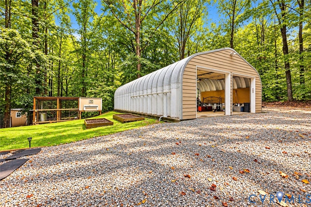 Quonset hut-style building with two overhead doors, gravel drive, manicured lawn, and raised garden beds