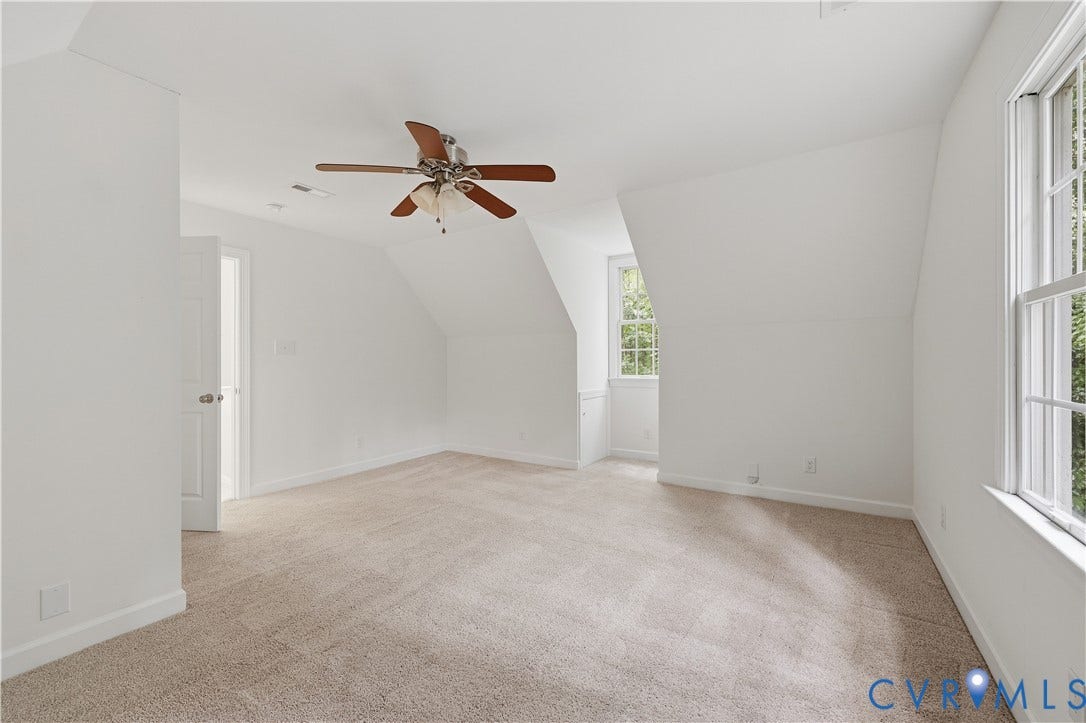 Carpeted flooring, sloped ceiling, ceiling fan, white paneled door, and multiple windows