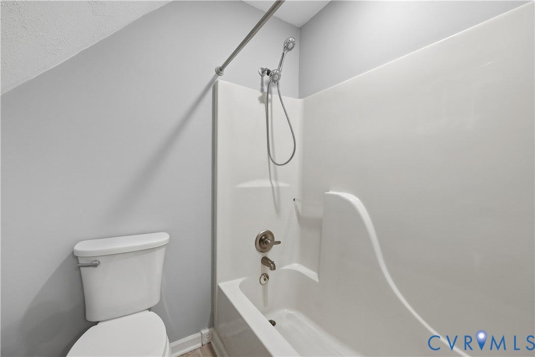 Bathtub with a shower insert and handheld showerhead, brushed nickel fixtures, and a white toilet