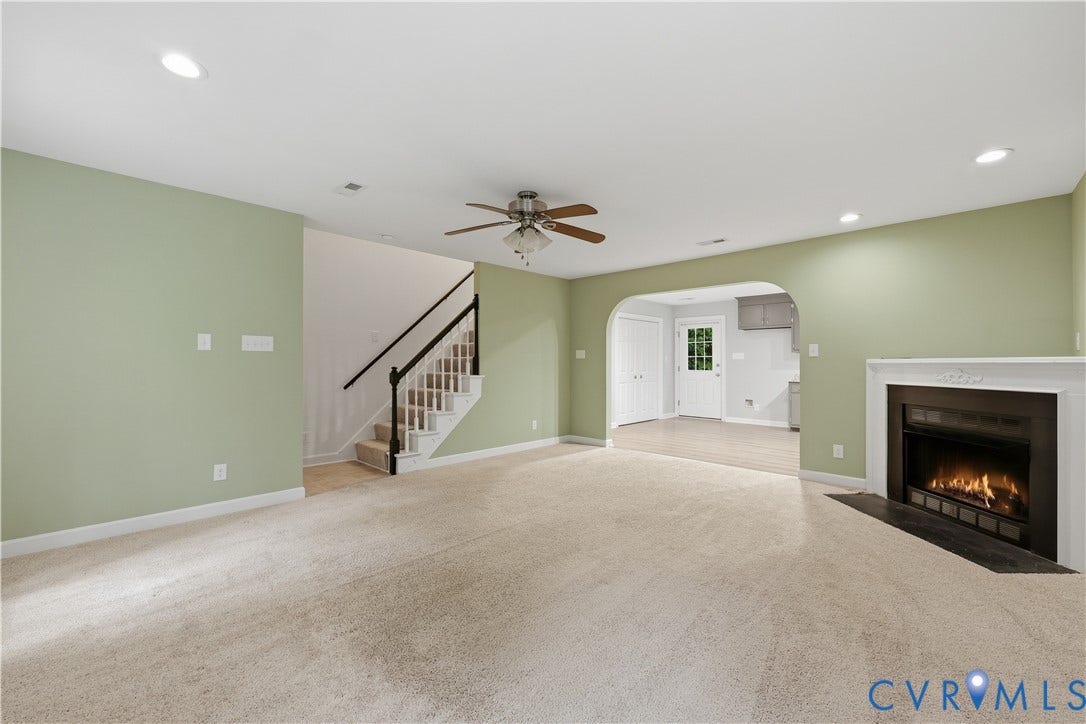 Recessed lighting, ceiling fan, white mantel fireplace with dark hearth, arched doorway, and staircase with dark handrail