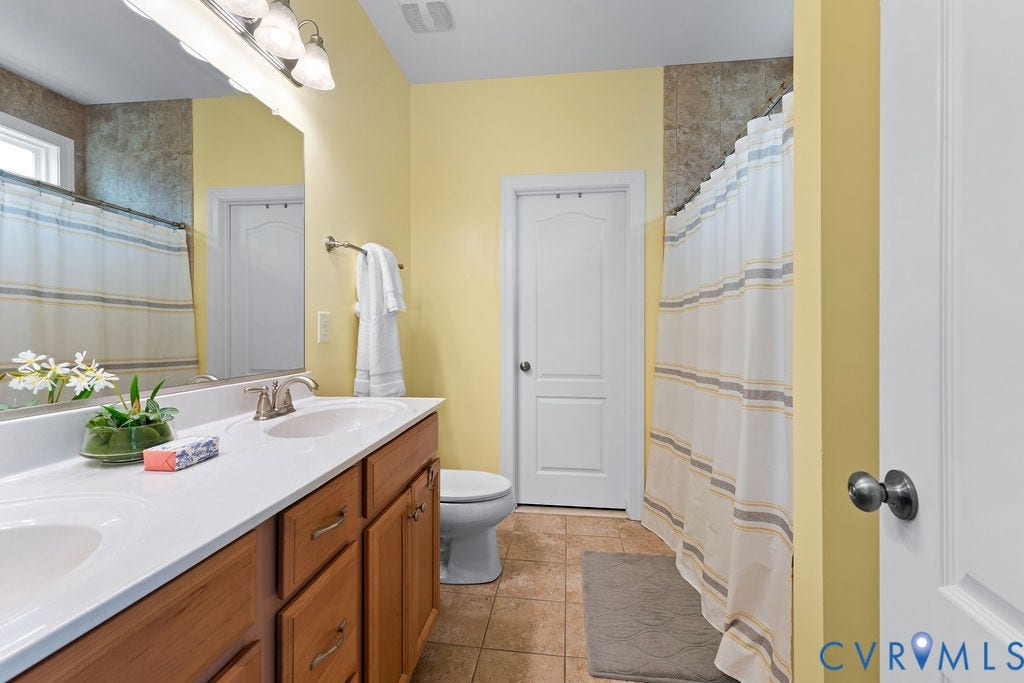 with ceramic tile floors and shower, walk-in shower with seat, two sink vanity, walk-in closet, and linen closet